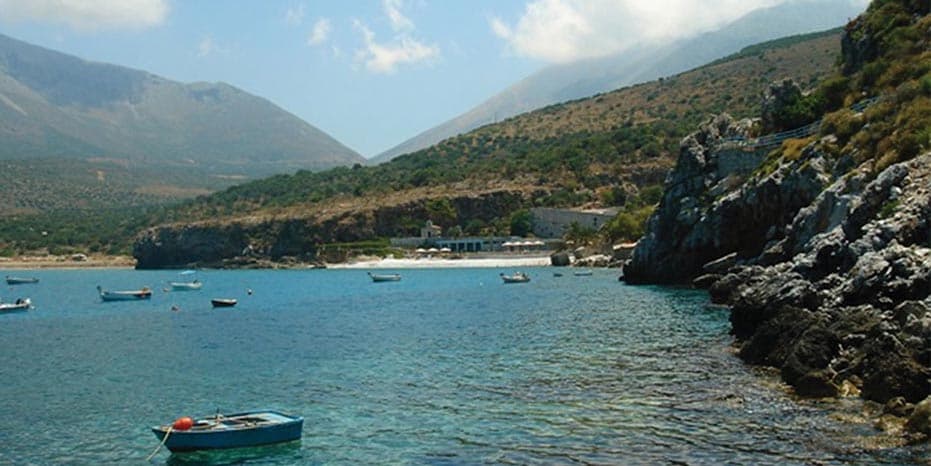 A coastline with cliffs, green hills, and blue water with a small sailboat