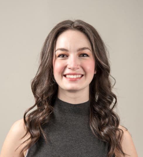 A smiling woman with long brown hair, wearing a gray sleeveless top