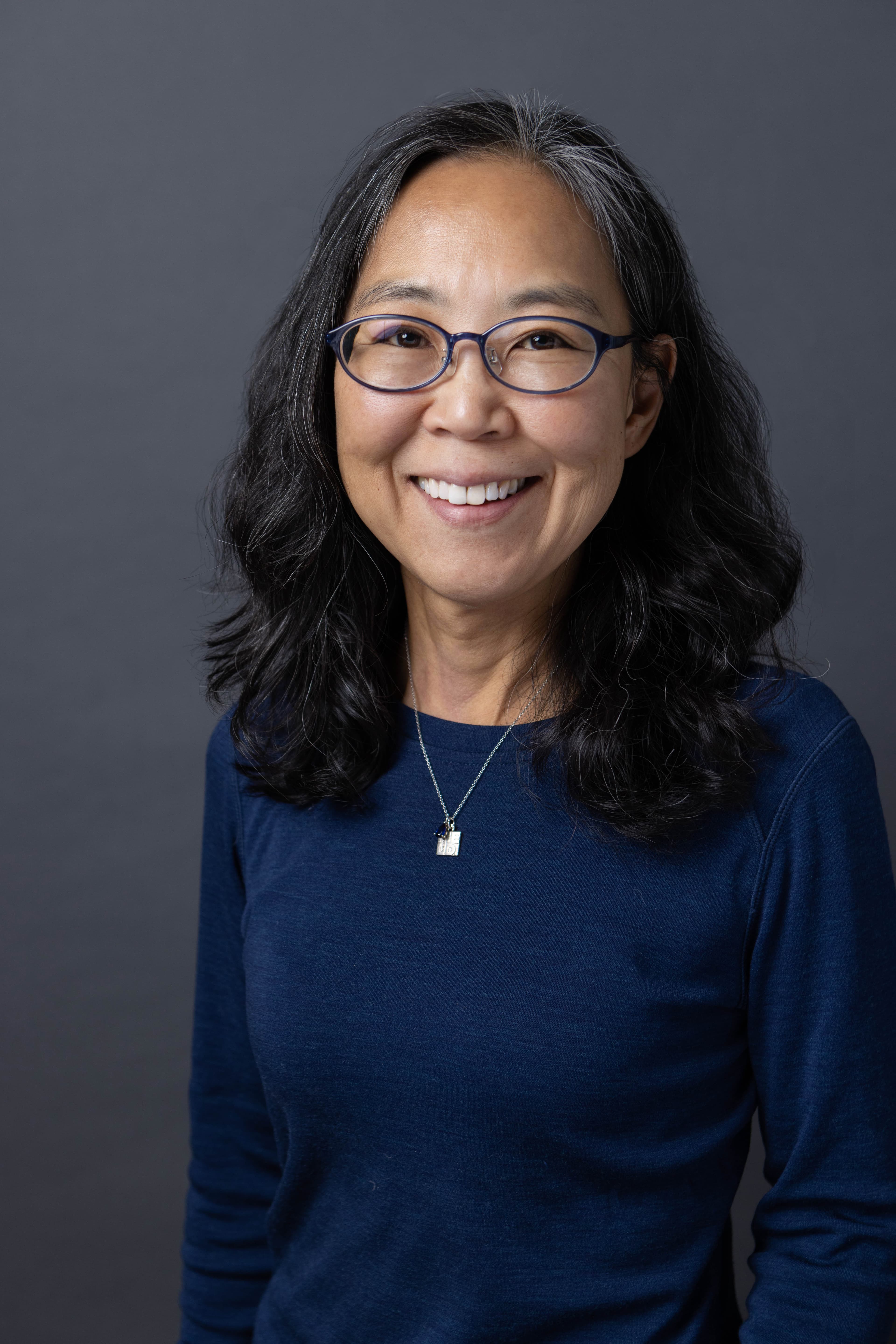 A woman wearing a blue top and glasses, smiling.