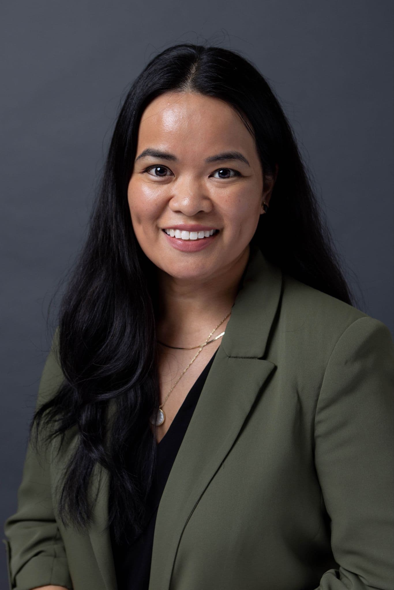 A woman with long black hair, wearing a black top and green jacket.