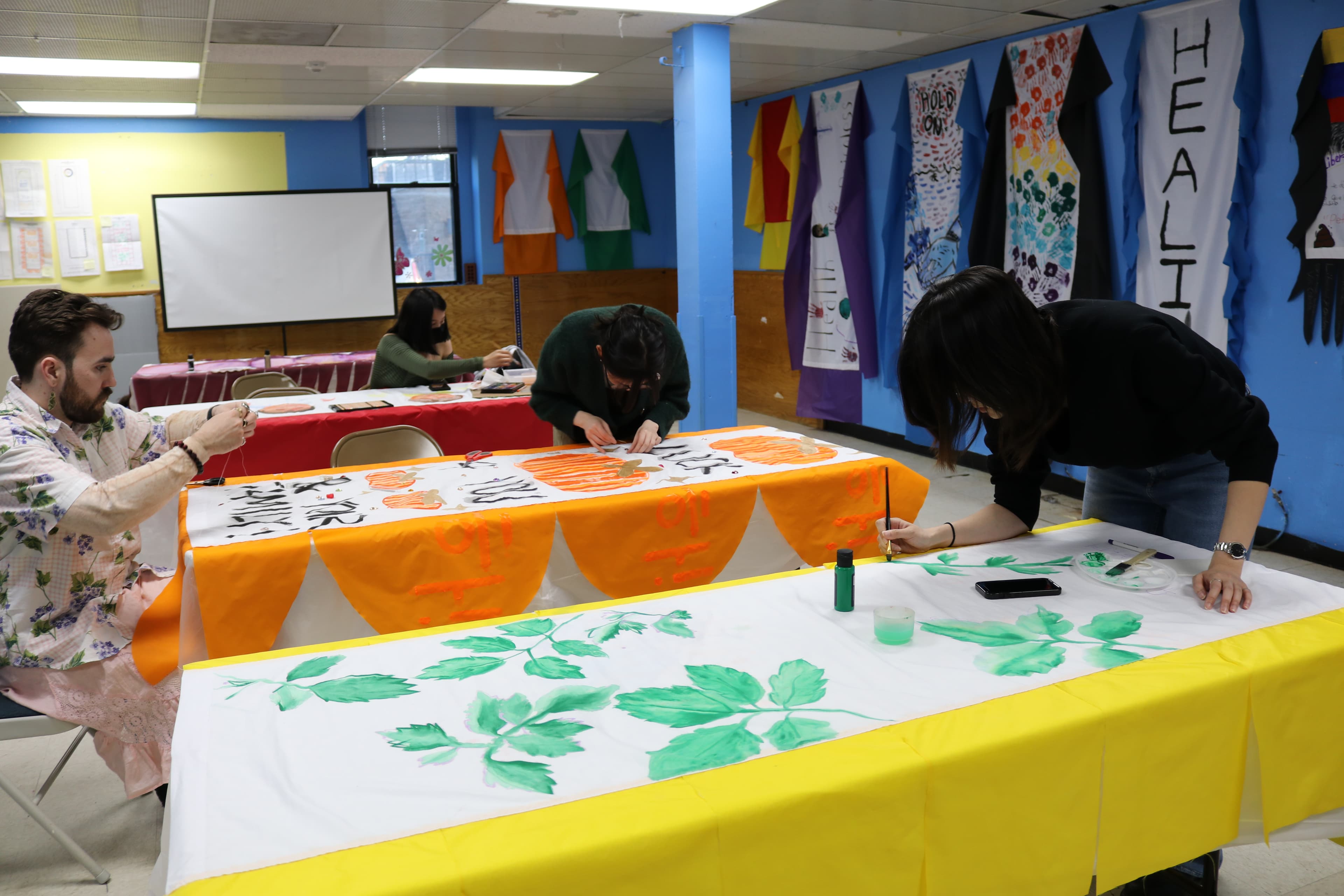 Several people painting on paper that is laid out on long tables.